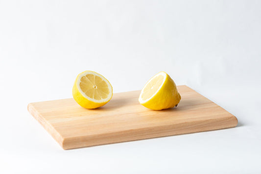 A small wooden cutting board with two lemon slices placed on it, set against a white background.