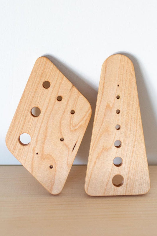 Two wooden herb stripper tools with different hole sizes for stripping herbs, one triangular and one parallelogram-shaped, placed on a wooden surface.