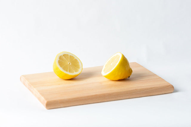 A small wooden cutting board with two lemon slices placed on it, set against a white background.